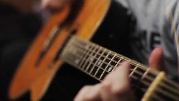 Un joven sintoniza una guitarra acústica arrancando las cuerdas y notas musicales — Vídeo de stock