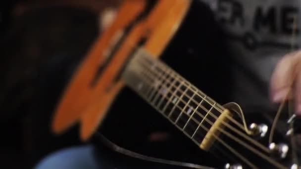 Un joven sintoniza una guitarra acústica arrancando las cuerdas y notas musicales — Vídeo de stock