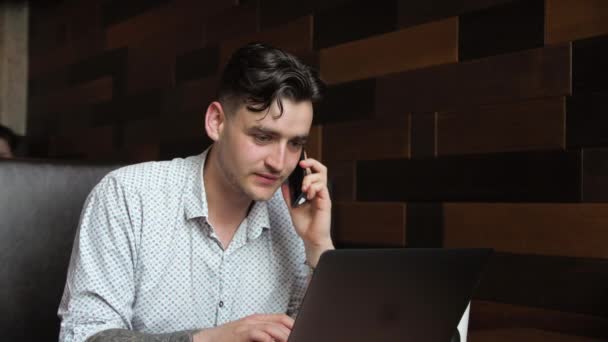 Чоловік брюнетка сидить в кафе за ноутбуком Робочі дослідження п'є каву Розмовляючи по телефону чат — стокове відео