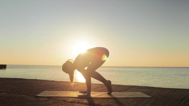 Kumsalda yoga yapan genç sarışın kadın güneşin doğuşunun ya da batışının arka planında — Stok video