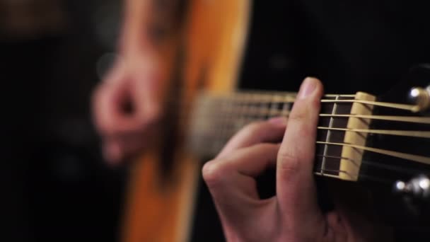 Un joven sintoniza una guitarra acústica arrancando las cuerdas y notas musicales — Vídeos de Stock