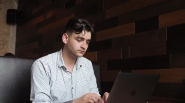 Serbest çalışan genç bir iş adamı esmer bir adam bir laptopun arkasında bir kafede oturuyor. Çalıştım, ders çalıştım, kahve içtim.