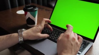 Serbest çalışan genç bir iş adamı esmer bir adam bir laptopun arkasında bir kafede oturuyor. Çalıştım, ders çalıştım, kahve içtim. Yakın plan. Yeşil ekran krom anahtarı.