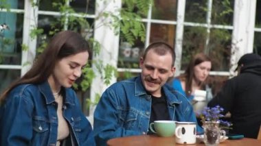 Genç bir çift. Denim giysileri. Eski bir restoranda randevuda, dışarıda. Konuşuyorlar..