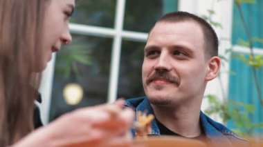 Genç bir çift. Denim giysileri. Eski bir restoranda randevuda, dışarıda. Makarna yiyorlar. Bir kadın erkeğini besler..