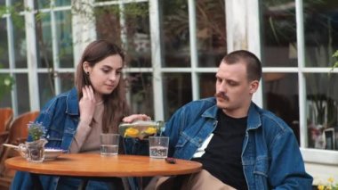 Genç bir çift. Denim giysileri. Eski bir restoranda randevuda, dışarıda. Konuşuyorlar..