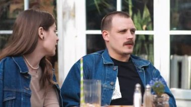 Genç bir çift. Denim giysileri. Eski bir restoranda randevuda, dışarıda. Konuşuyorlar. Sallanıyorlar.