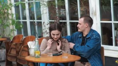 Genç bir çift. Denim giysileri. Eski bir restoranda randevuda, dışarıda. Konuşuyorlar..