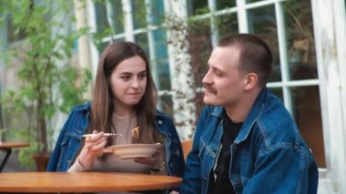 Genç bir çift. Denim giysileri. Eski bir restoranda randevuda, dışarıda. Konuşuyorlar. Sallanıyorlar.