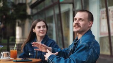 Genç bir çift. Denim giysileri. Eski bir restoranda randevuda, dışarıda. Konuşuyorlar. Sallanıyorlar.