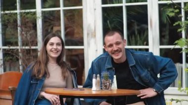 Genç bir çift. Denim giysileri. Eski bir restoranda randevuda, dışarıda. Konuşuyorlar. Sallanıyorlar.