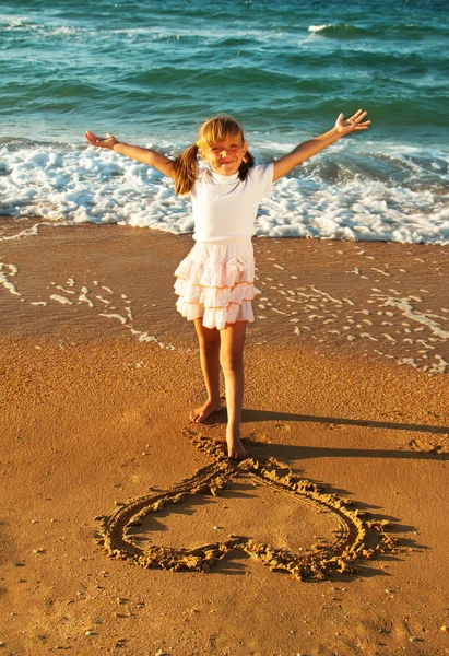 Girl at the beach drawing heart on a sand — Stock Photo, Image