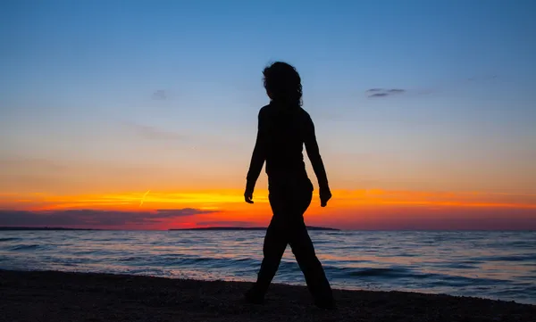 Kvinna promenader på stranden vid solnedgången — Stockfoto