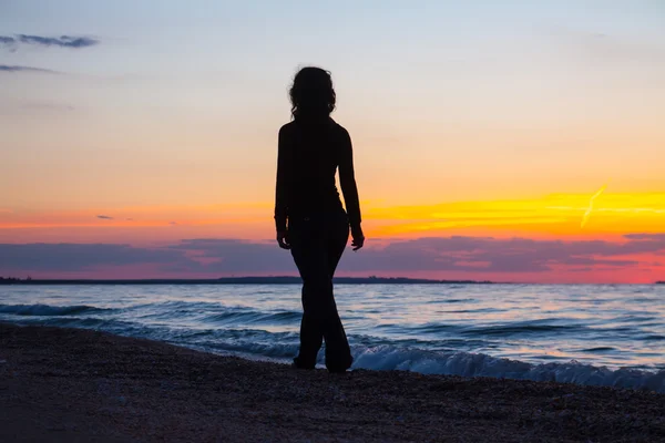 日没時に海岸を歩く女性は — ストック写真