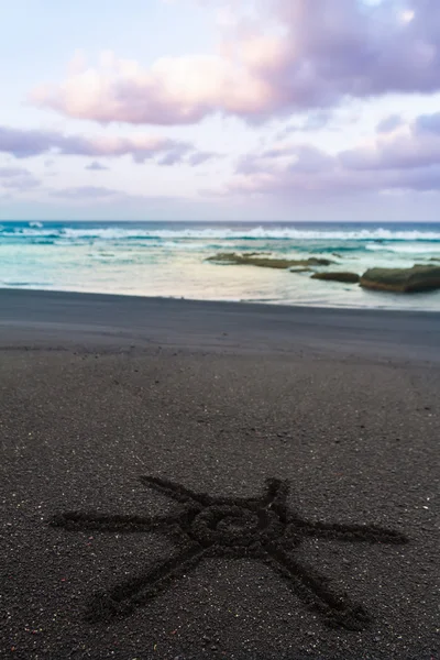 Sun sign drawn on black sand of beach — Stock Photo, Image