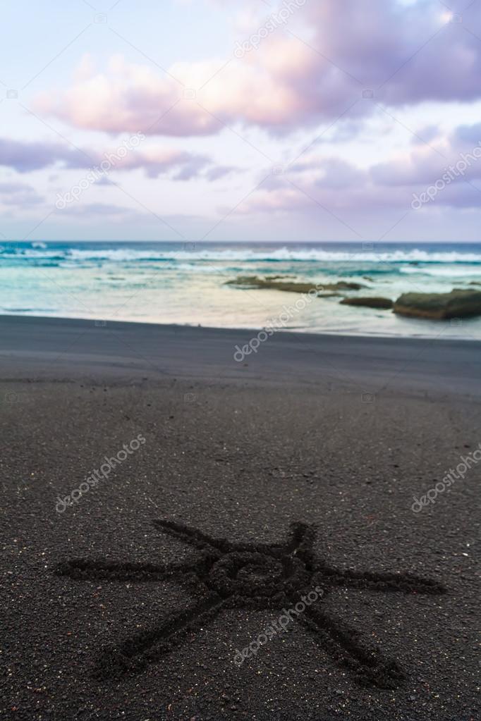Sun sign drawn on black sand of beach
