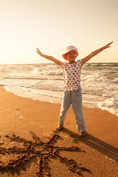 Маленькая девочка рисует солнце на песке на пляже — стоковое фото