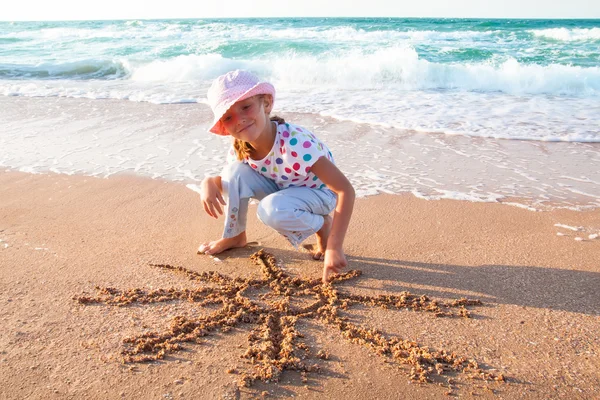 Menina desenha sol na areia na praia — Fotografia de Stock