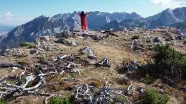 Dağın tepesindeki kırmızı elbiseli kadına drone görüntüsü. Güzellik, zafer, başarılar