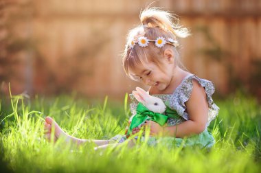 Cute little girl with a bunny rabbit has a easter at green grass clipart