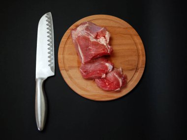 Yuvarlak ahşap kesme tahtası ve bıçakla dilimlenmiş domuz filetosu, siyah arka planda izole edilmiş..