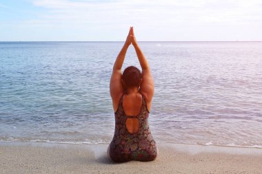 Ayyaş kadın deniz kenarında yoga yapıyor, doğada meditasyon, tonlu fotoğraf, arka görüş.