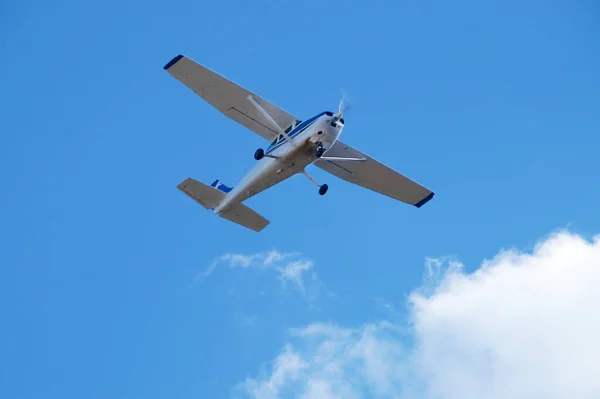 Temiz bir gökyüzü ve beyaz bulutların arka planında küçük tek motorlu uçak, alt görünümü yakın