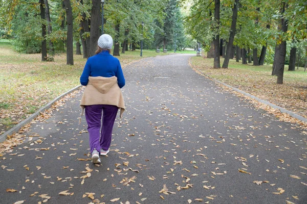 Yaşlı bir kadın sonbahar parkında tek başına yürüyor.