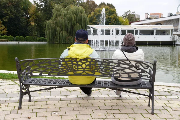 男と女は公園のベンチに座って噴水のある池を見て — ストック写真