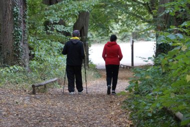 Erkekler ve kadınlar parkta sopalarla yürüme pratiği yapıyorlar.