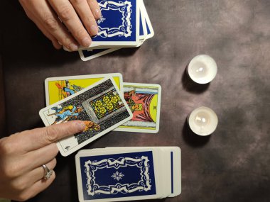 Falcı, mum ışığında tarot kartlarını katlıyor, yukarıdan yakın plan.
