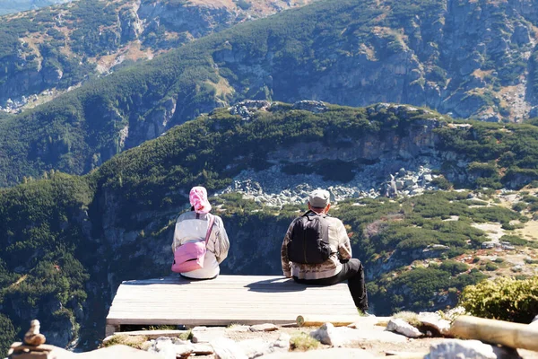 Erkek ve kadın dağın tepesinde oturur ve dağ manzarasının arkasından bakar..