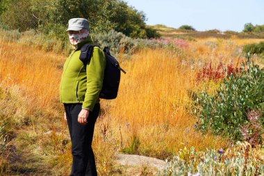 male traveler in a medical mask with a backpack outdoors.