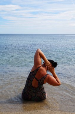 Kıvrımlı bir kadın deniz kıyısında egzersiz yapıyor, dikiz aynasından..