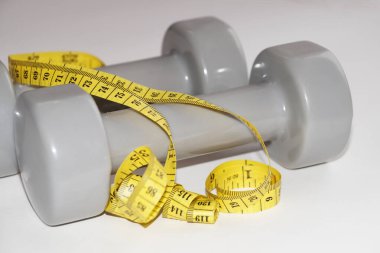 Beyaz arka planda iki gri dambıl ve bir santimetre..