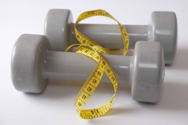 Beyaz arka planda iki gri dambıl ve bir santimetre..