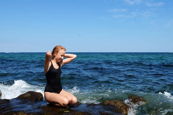 黒の水着姿の赤髪の10代の少女が地平線を背景に海岸に座り — ストック写真