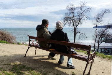 Baba ve kız bir bankta oturup denize, arka manzaraya bakıyorlar.