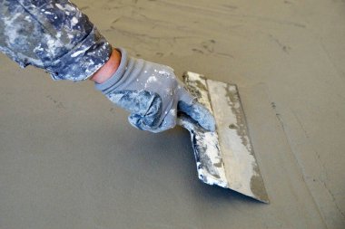 Spatulalı bir adamın eli yere saçılmış çimentoyu düzleştirir..
