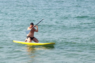 Adam denizdeki SUP tahtasının üstünde kürekle diz çöküyor..