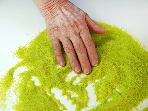 Sand therapy as a rehabilitation after a stroke, the hand of an elderly woman close-up on the green kinetic sand. Alternative therapy to improve fine motor skills.