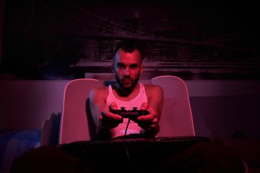 30 yaşında elinde joystick olan bir adam bilgisayar oyunları oynuyor, çeşitli duygular yaşıyor. Evdeki kanepede oturuyor. TV tarafından görünüm.