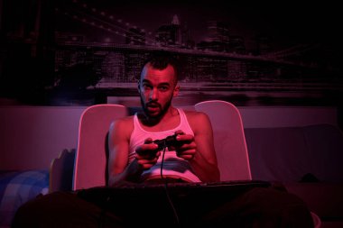 30 yaşında elinde joystick olan bir adam bilgisayar oyunları oynuyor, çeşitli duygular yaşıyor. Evdeki kanepede oturuyor. TV tarafından görünüm.