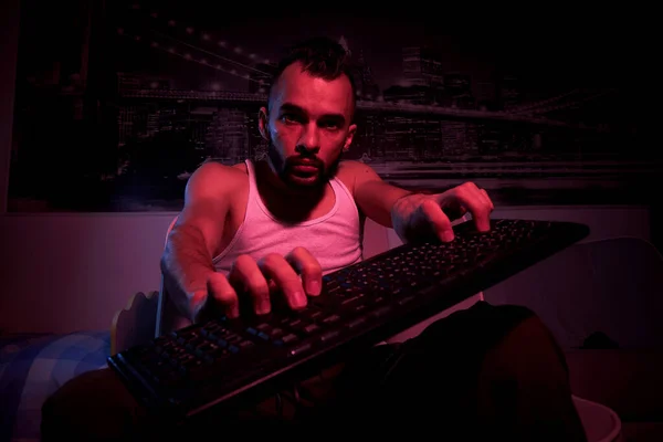 a gamer of thirty years old with a keyboard in his hands plays computer games, gets angry, feels indignation, various emotions. view from the TV side.