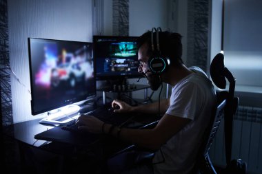 30 yaşındaki genç bir oyuncu bilgisayar başında oturmuş, oyun oynuyor, sinirli, sinirli, endişeli. Düşük odaklı seçici odaklı..