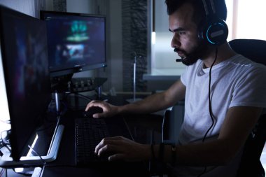 30 yaşındaki genç bir oyuncu bilgisayar başında oturmuş, oyun oynuyor, sinirli, sinirli, endişeli. Düşük odaklı seçici odaklı..