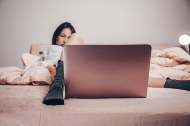 Genç bir Asyalı web kamerası mankeni dizüstü bilgisayarın önünde bacaklarını açarak yatıyor. Cazibesini gösteriyor. düşük odak derinliği, seçici odak.