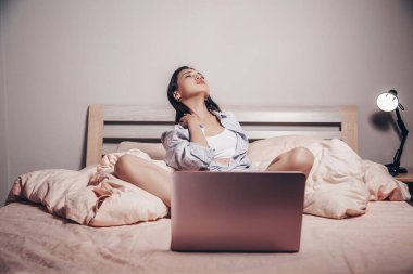 Genç bir Asyalı web kamerası mankeni dizüstü bilgisayarın önünde bacaklarını açmış oturuyor. İletişim kuruyor ve cazibesini gösteriyor. Düşük odak derinliği, sanatsal fotoğraf işleme.