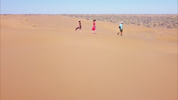 Três viajantes caminham pelo deserto em cima de dunas de areia — Vídeo de Stock