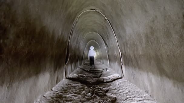 Un bambino corre attraverso un tunnel di cemento nella luce — Video Stock